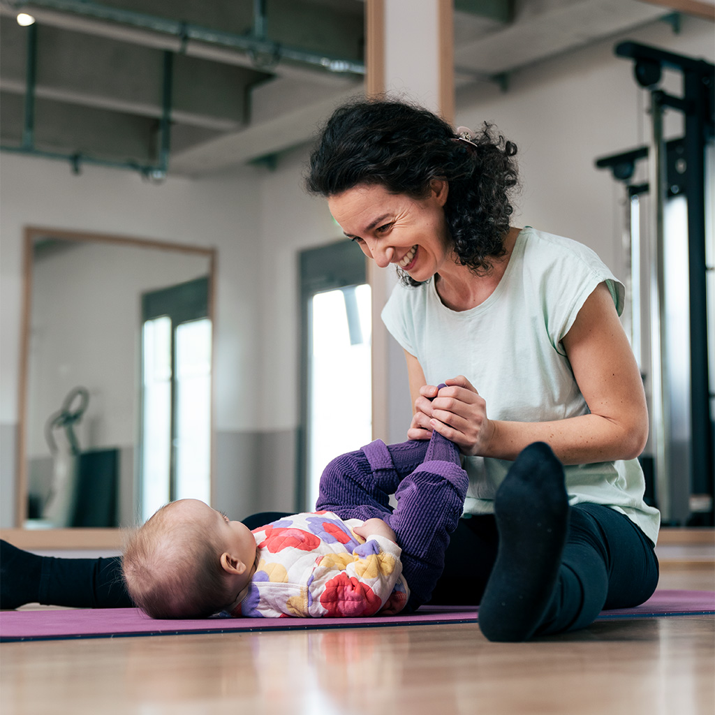 In einem liebevoll eingerichteten Studio hält eine Babymassage-Trainerin die kleinen Hände eines Babys sanft in ihren Händen und massiert sie behutsam.
