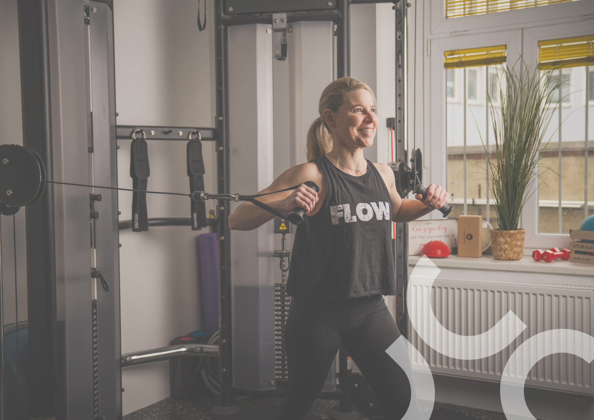 Janine, die am Krafturm eine Ruderübung ausführt, mit fokussiertem Blick und kraftvollem Zug in einem modernen Trainingsraum.