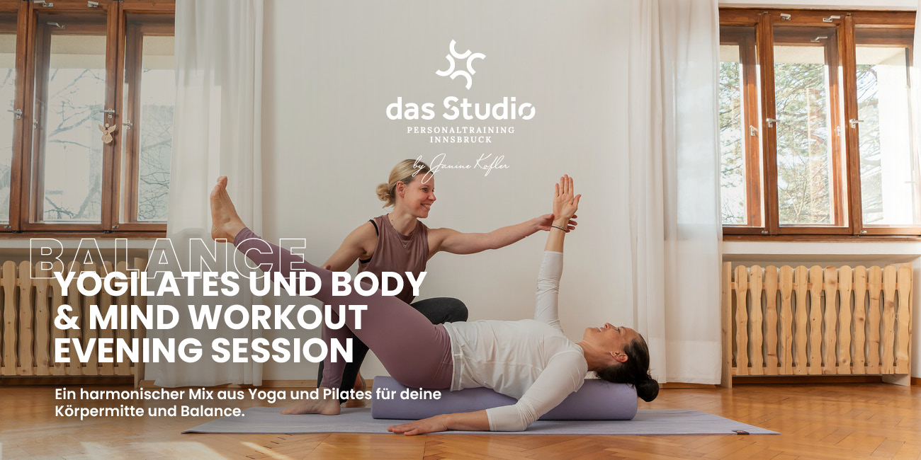 Eine Trainerin unterstützt eine liegende Person bei einer Yogilates-Übung in einem hellen Raum mit großen Fenstern und warmem Holzboden.